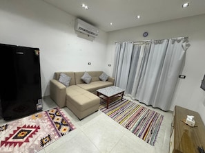 A living room with a sofa, a coffee table, a TV, and a refrigerator. - Your Perfect Getaway in Naama Bay, Sharm El Sheikh! (South Sinai Governorate)