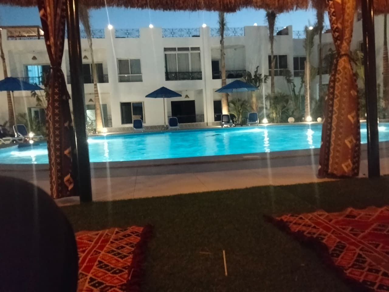 A pool area with lounge chairs and umbrellas, a building with balconies, and a night-time setting.