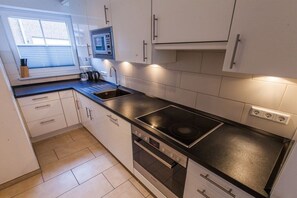 Eine kleine Küche mit Backofen, Kochfeld und einem Fenster mit Jalousien.