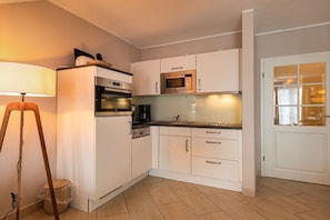 A compact kitchen with white cabinets, a microwave, an oven, and a sink. - Holiday apartment in Binz with swimming pool (Binz)