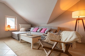 A cozy loft bedroom with a sloped ceiling, a sofa with patterned cushions, a wooden coffee table, and a floor lamp. - Holiday apartment in Binz with swimming pool (Binz)