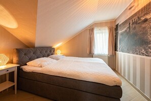 A bedroom with a bed, bedside table, lamp, and a window with curtains. - Holiday apartment in Binz with swimming pool (Binz)