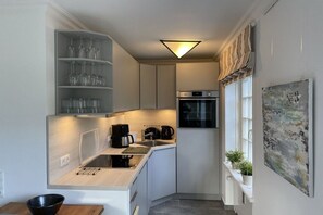 Una cocina compacta con horno integrado, cafetera y ventana con plantas.