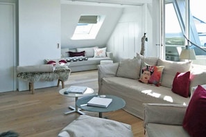 A modern living room with a sofa, a coffee table, and a bench. There is a skylight above the sofa and a view of the outside. - Holiday apartment with 2 bedrooms (Hörnum)