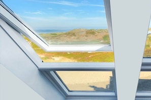 Une lucarne offrant une vue sur un paysage verdoyant et des collines lointaines.