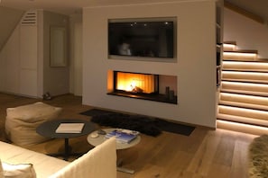 A modern living room with a fireplace, a flat-screen TV mounted above it, and a staircase with wooden steps. - Holiday apartment with 2 bedrooms (Hörnum)