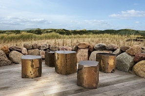 Terrasse extérieure en bois, agrémentée de jardinières en pierre et offrant en arrière-plan un paysage de dunes.