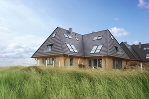 A modern house with a sloped roof, large windows, and a grassy foreground. - Holiday apartment with 2 bedrooms (Hörnum)