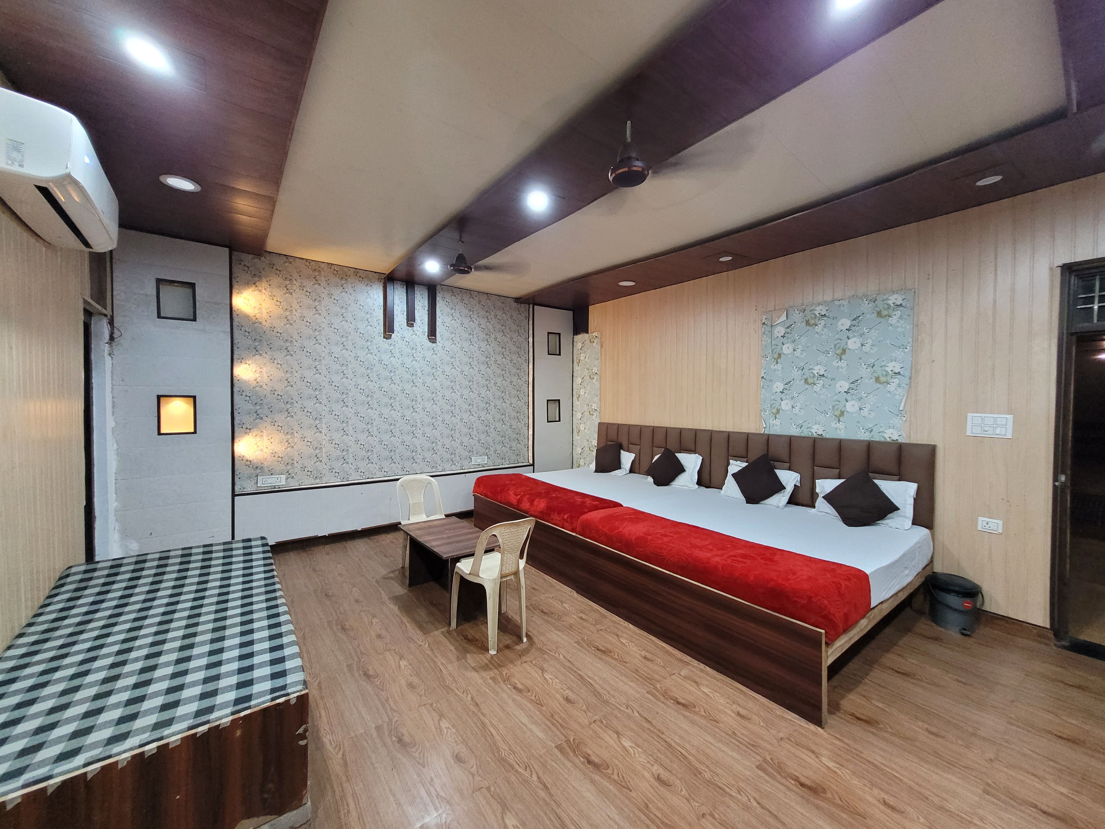 Quarto de hotel com uma cama grande, escrivaninha, cadeira, ventilador de teto e ar condicionado fixado na parede.