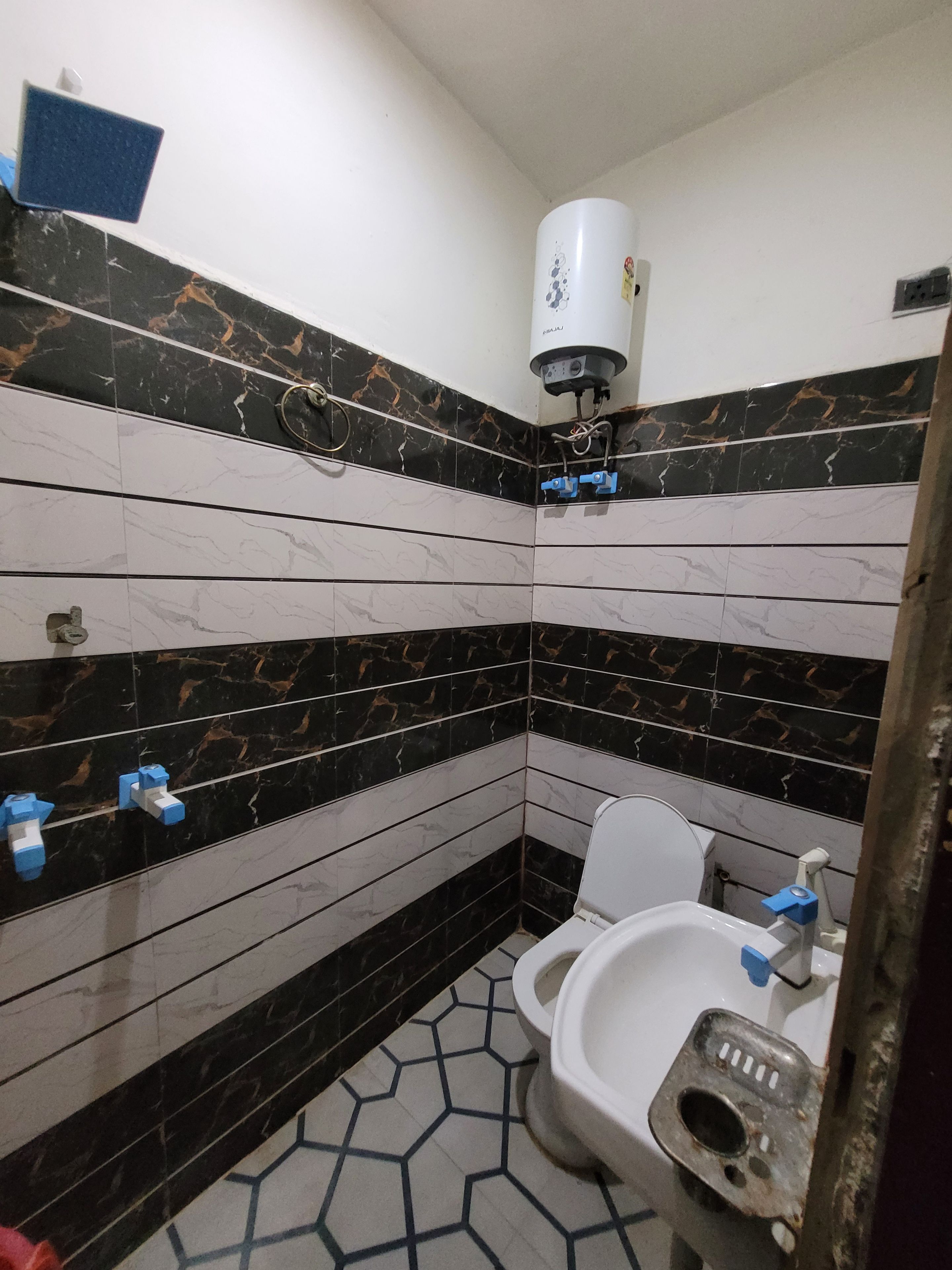 Un bany amb parets revestides de rajoles negres i blanques, un vàter blanc i un lavabo amb un aireix blau.