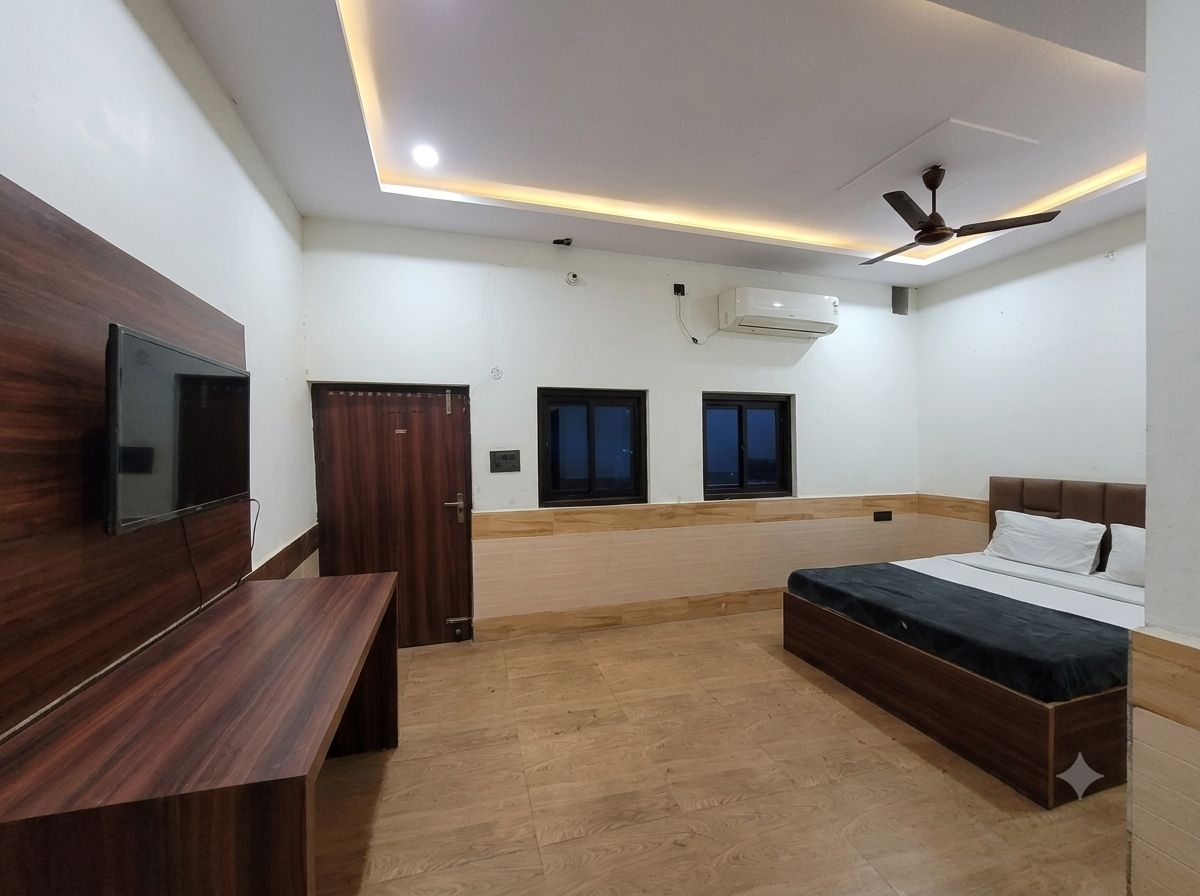 A bedroom with a bed, a TV, a ceiling fan, and a window.