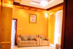 Una habitación con un sofá color beige, una lámpara de araña y un cuadro en la pared.