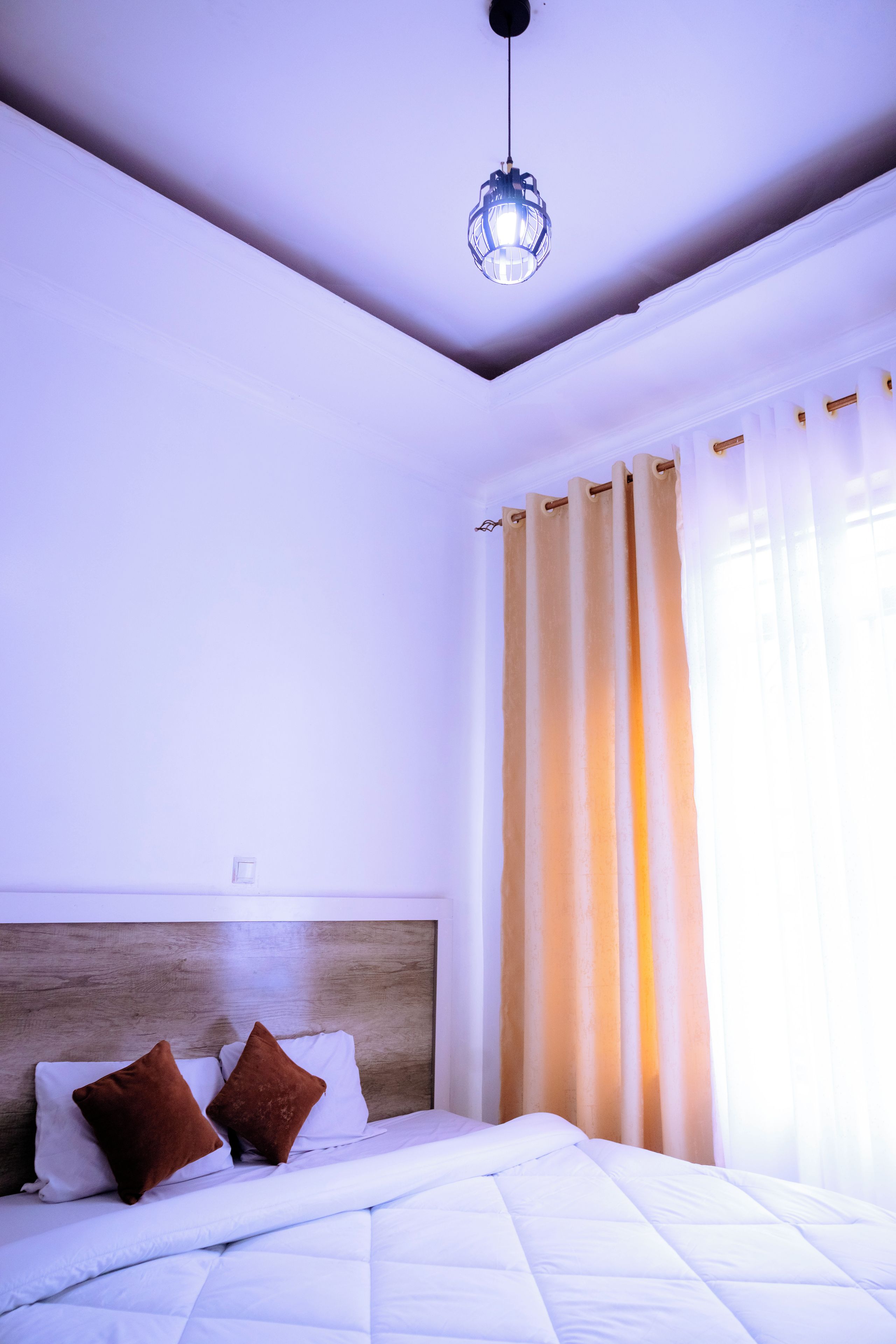 Een slaapkamer met een bed, gordijnen en een hanglamp.