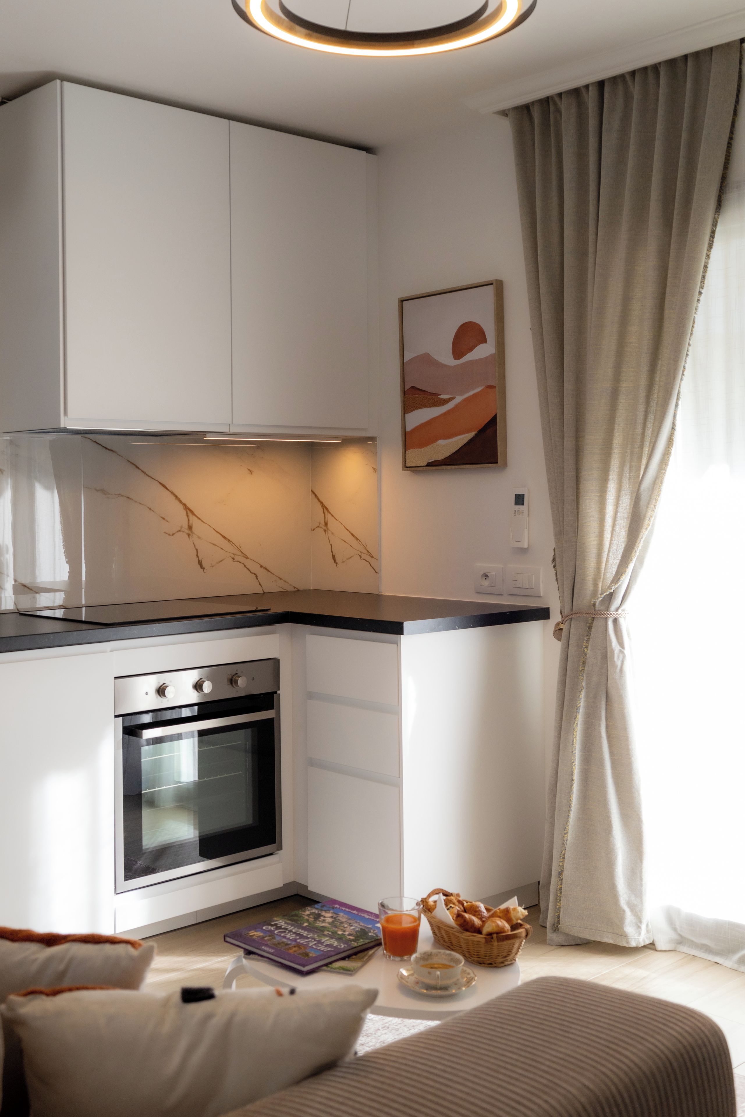 A modern kitchen with white cabinetry, a built-in oven, and a marble backsplash.