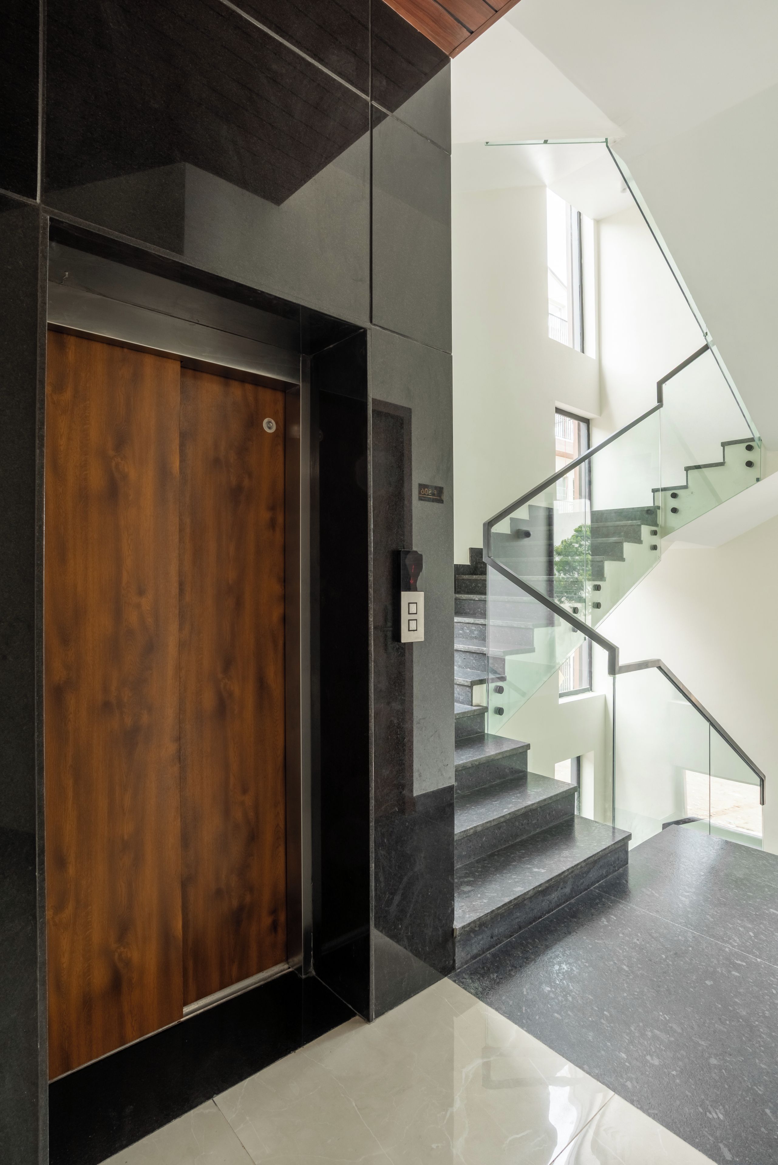 Un interior moderno con una puerta de madera, una escalera con barandas de cristal y un diseño limpio y minimalista.