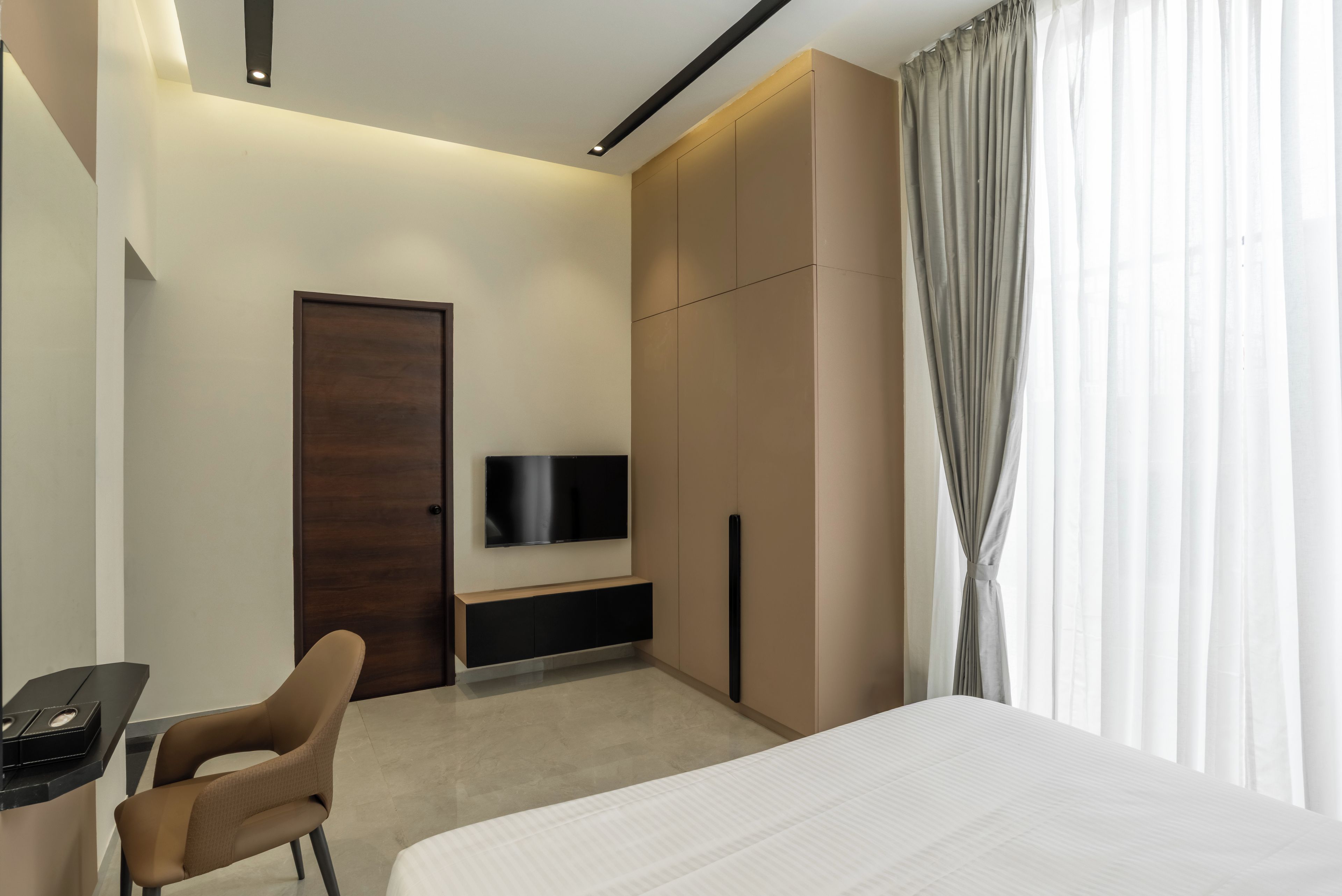 A modern hotel room with a bed, a desk, a chair, a TV, and a wardrobe.