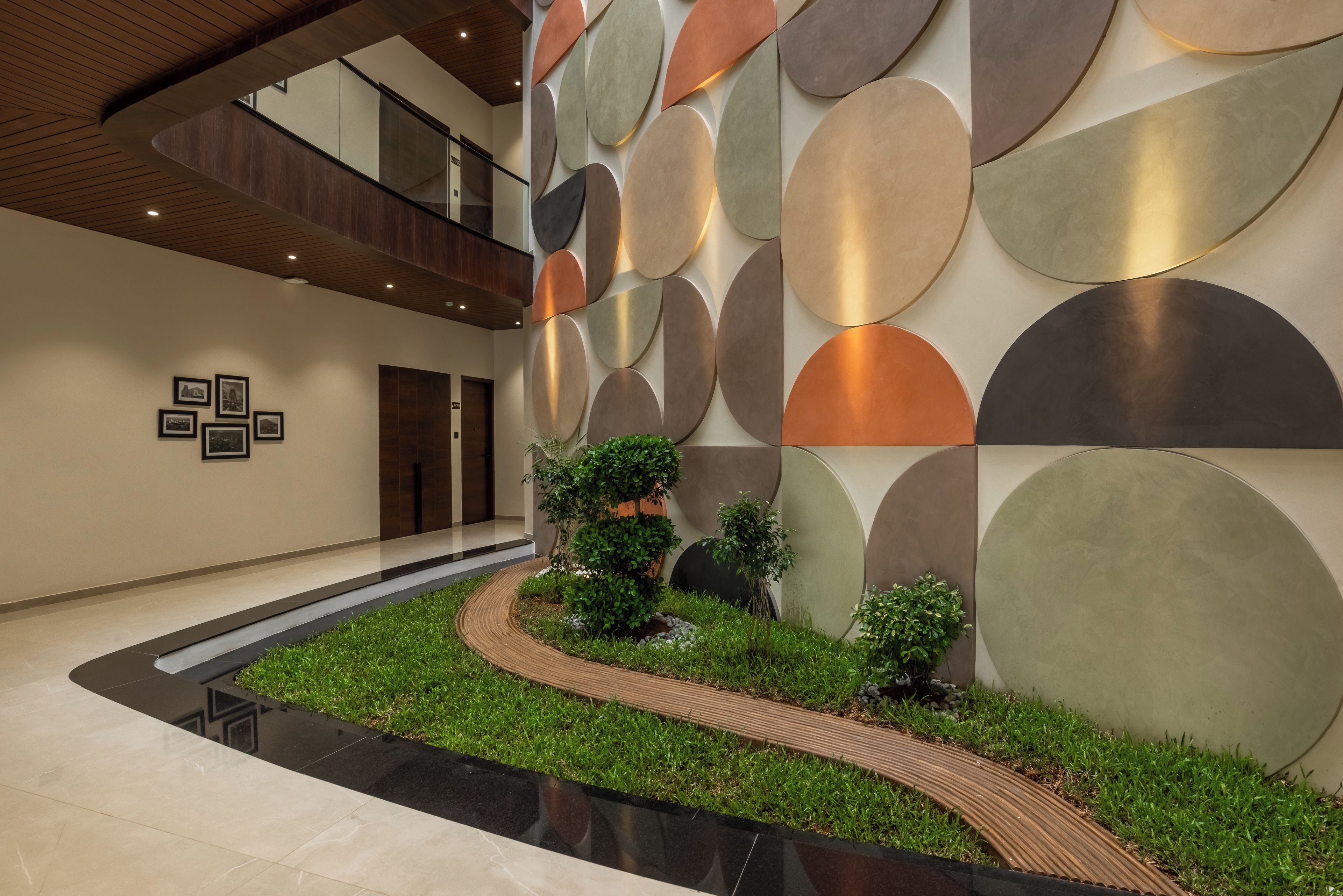 A modern lobby with a curved pathway, a wall with abstract circular patterns, and a small garden area.