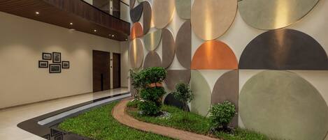A modern lobby with a curved pathway, a wall with abstract circular patterns, and a small garden area.
