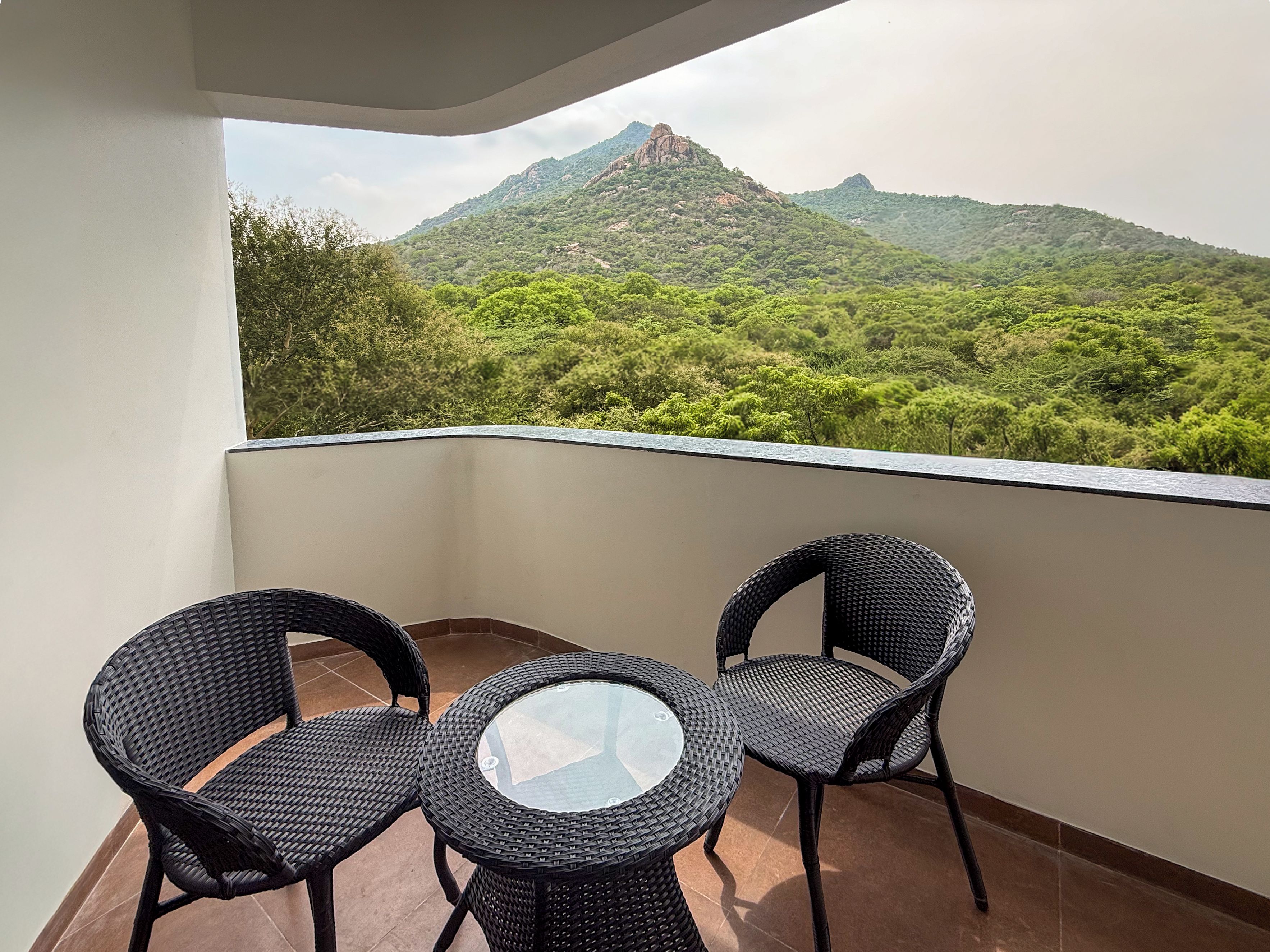 Un balcón con dos sillas de mimbre y una mesa de vidrio, con vistas a un paisaje montañoso.