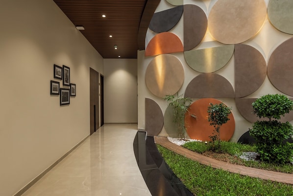 Un pasillo moderno con piso pulido, una serie de decoraciones circulares en la pared y un pequeño jardín con plantas y un borde de madera.