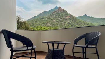Un balcón con tres sillas de mimbre y una pequeña mesa, con vistas a un paisaje montañoso.