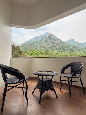Un balcón con tres sillas de mimbre y una mesita redonda, con vistas a un paisaje montañoso.