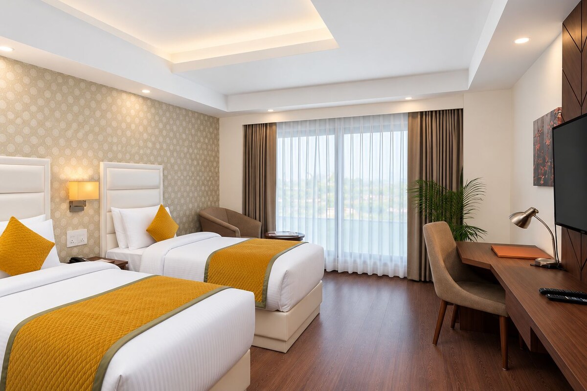 Une chambre d’hôtel avec deux lits, un bureau, une chaise, une télévision et une grande fenêtre avec des rideaux.