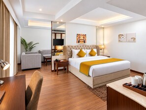 Une chambre d’hôtel équipée d’un lit, d’un bureau, d’une chaise, d’un canapé, d’une télévision et d’une plante.