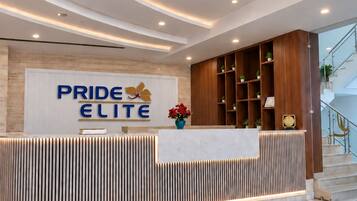 Zona de recepción de hotel con diseño moderno, que incluye una gran lámpara de araña, un mostrador de recepción con el letrero 'PRIDE ELITE' y un diseño decorativo en el suelo.