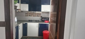 A compact kitchen with a gas stove, a red trash bin, and a water dispenser. - Cozy 2-bedroom apartment in peaceful Bahawalpur with AC and gym (Bahawalpur)