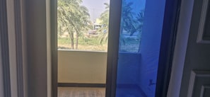 A view through a window with a view of palm trees and a building in the distance. - Cozy 2-bedroom apartment in peaceful Bahawalpur with AC and gym (Bahawalpur)