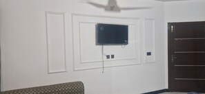A room with a ceiling fan, a mounted television, and a door.