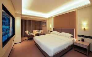 Habitación de hotel con una cama grande, un escritorio, una silla y un televisor en la pared.
