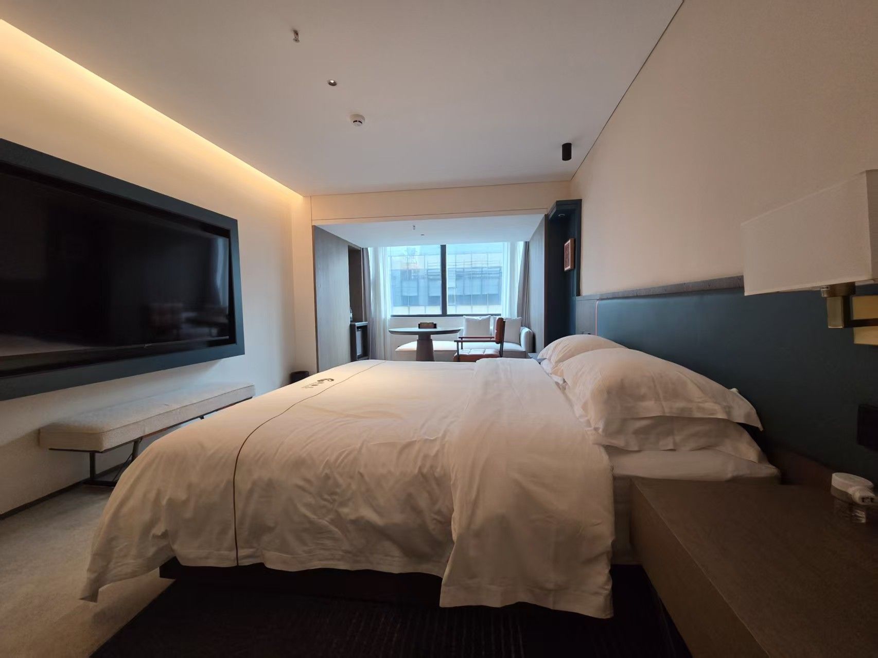 A hotel room with a large bed, a TV, a desk, and a window with a view.