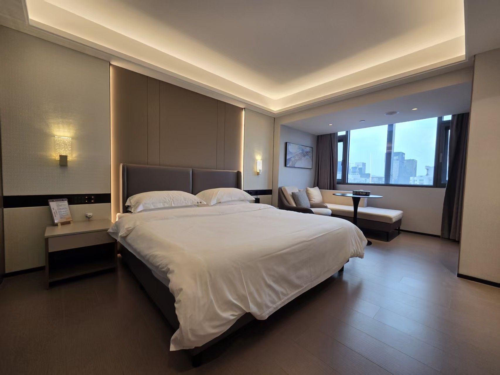 A modern hotel room with a large bed, a desk, and a view of the city.