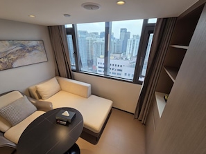 Habitación de hotel moderna con sofá, una pequeña mesa y vistas de la ciudad a través de grandes ventanales.