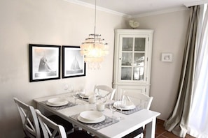 A dining area with a white table set for four, a chandelier, and a cabinet with glass doors. - at the Arnfried country house (Wenningstedt)