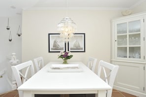 A dining area with a white table, chairs, a chandelier, and a cabinet with glass doors. - at the Arnfried country house (Wenningstedt)
