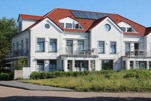 A multi-story residential building with a red-tiled roof, balconies, and a paved driveway. - Holiday apartment with 2 bedrooms (Norderney)