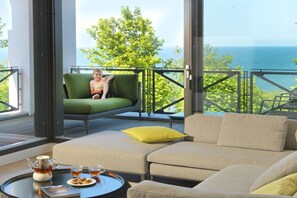 Ein Balkon mit einer Couch und einem Tisch, gedeckt mit Tee und Snacks, mit Blick auf ein Gewässer.