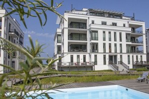 Ein modernes, mehrstöckiges Gebäude mit Balkonen, einem Poolbereich und einer Holzterrasse.