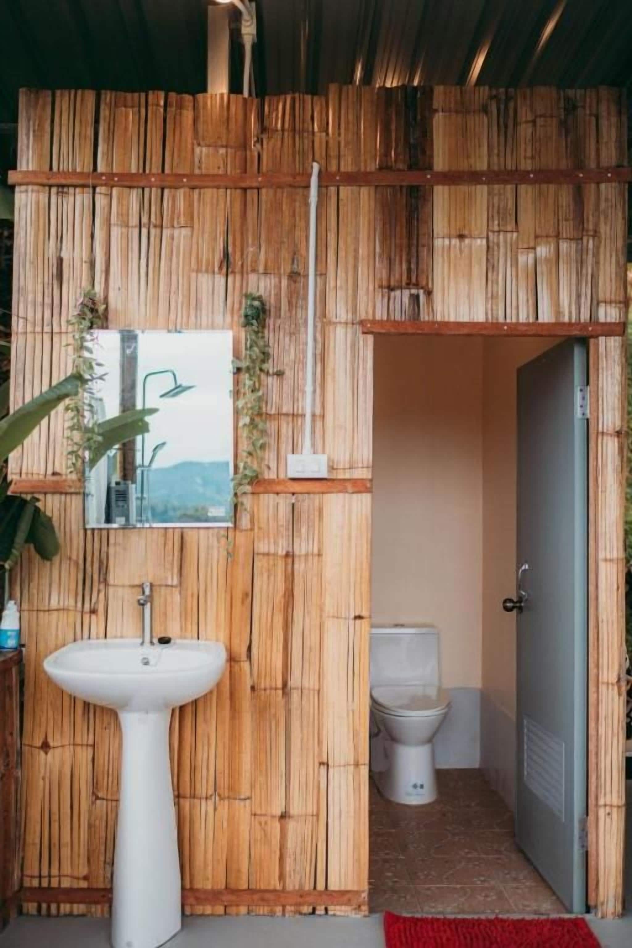 Et badeværelse med en væg af bambus, en hvid vask og et toilet.