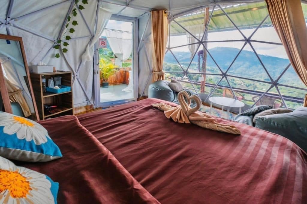 Alojamiento con tienda de campaña, cama, almohadas, una mesita y vistas al exterior.