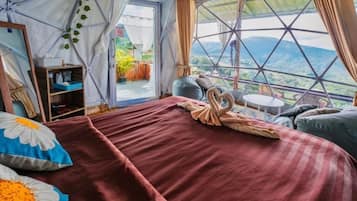 Alojamiento con tienda de campaña, cama, almohadas, una mesita y vistas al exterior.
