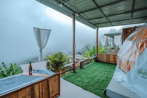 A covered outdoor area with a hot tub, a wooden bench, and a tent.