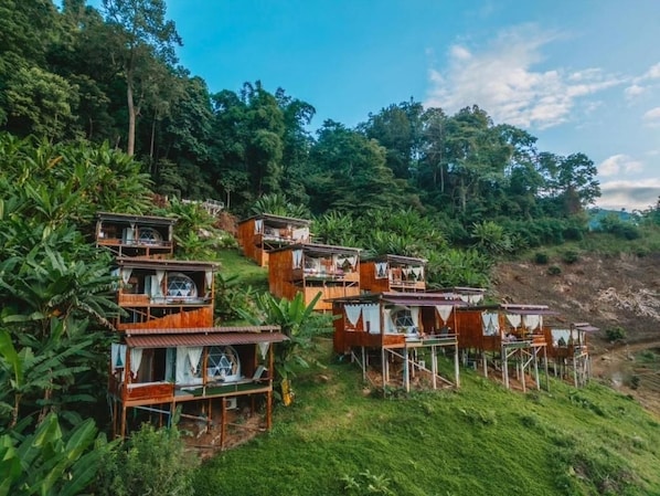 A series of wooden cabins with multiple levels, surrounded by lush greenery and trees.