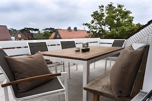 Um pátio externo com mesa e cadeiras de madeira, cercado por um muro branco.
