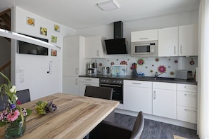 A modern kitchen with white cabinets, a microwave, and a stove. There's a dining table with chairs and a vase of flowers. - Holiday home in Cuxhaven with swimming pool (Cuxhaven)