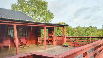 A wooden deck with red railings, a covered seating area with chairs, and a potted plant.