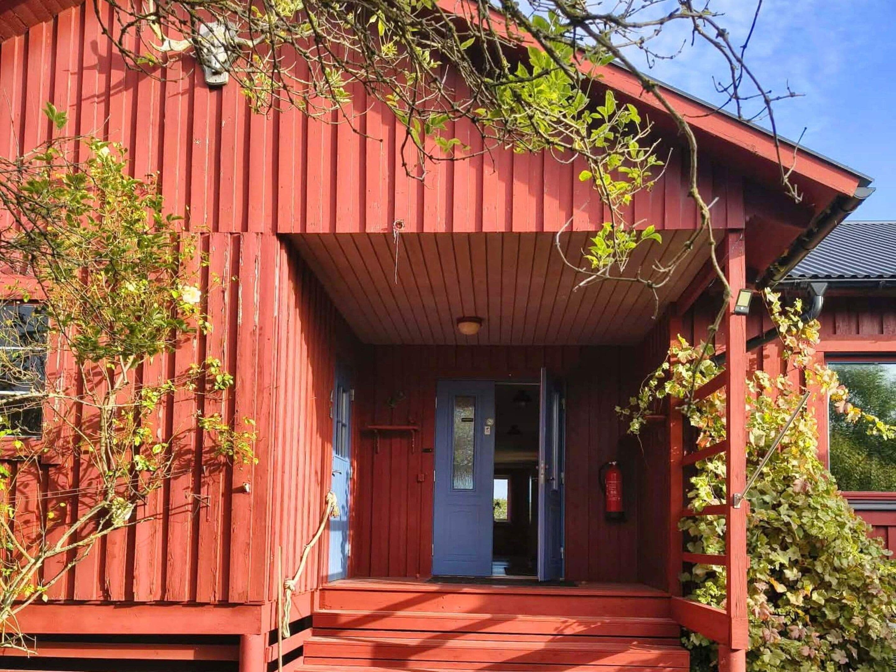 A red wooden building with a porch, a blue door, and a fire extinguisher mounted on the wall.